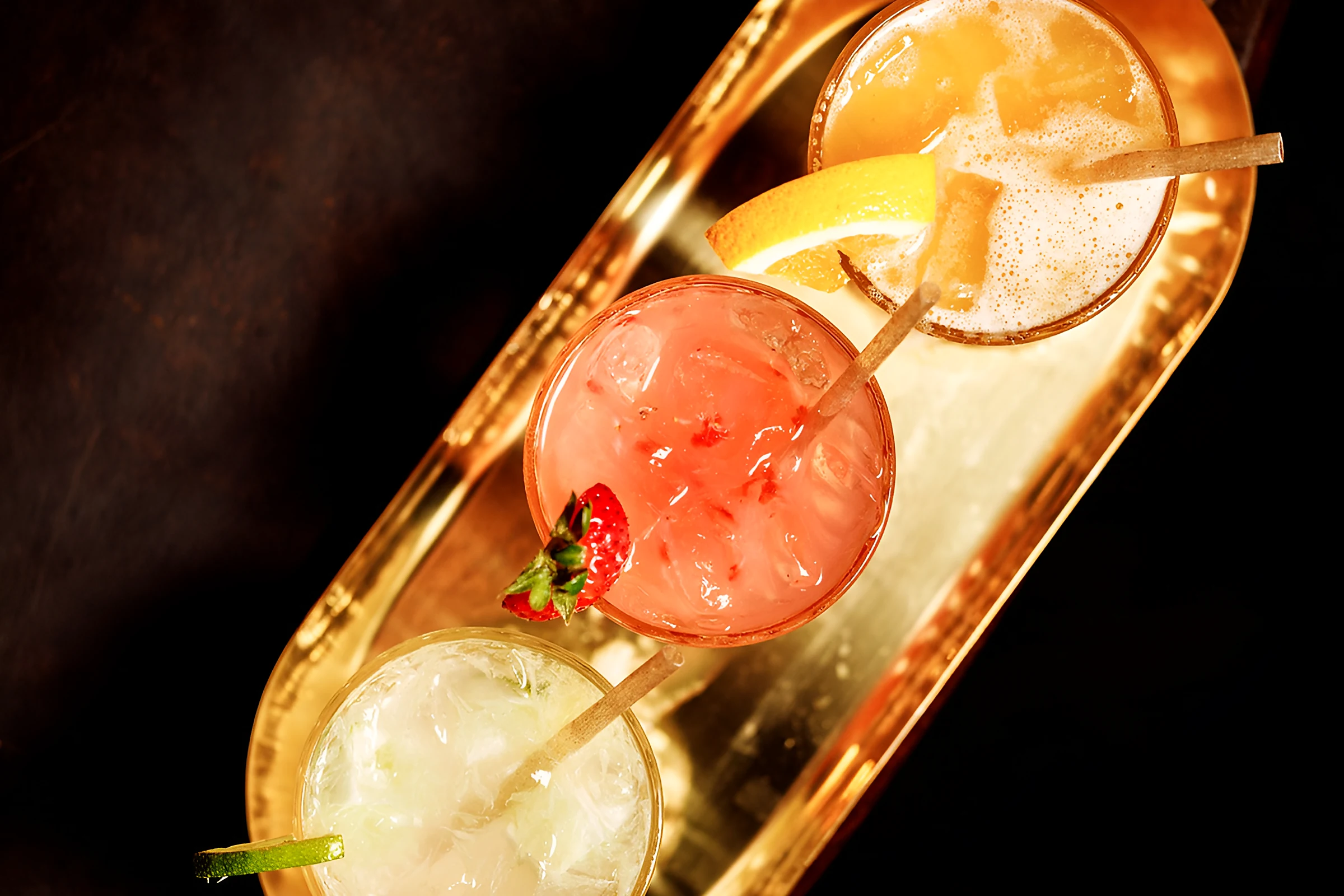 Three craft cocktails on a golden tray