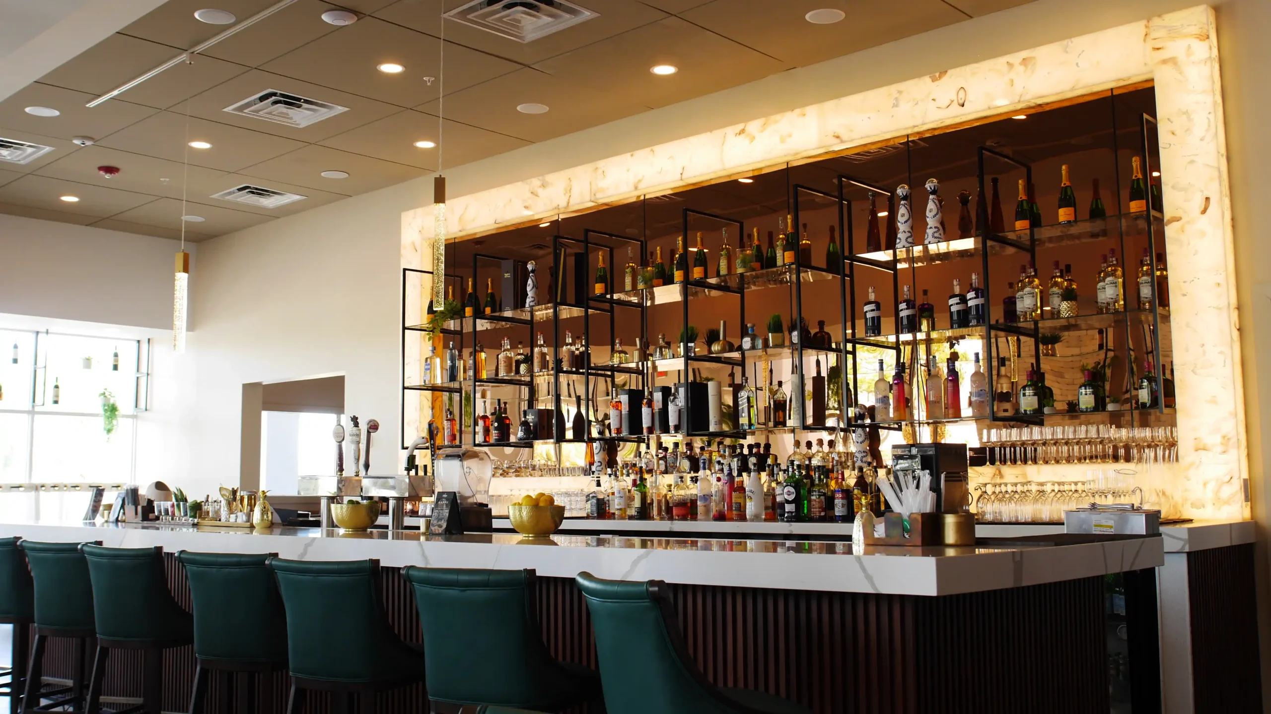 The bar at Adega Gaucha Kissimmee with a glowing back bar and green velvet stools