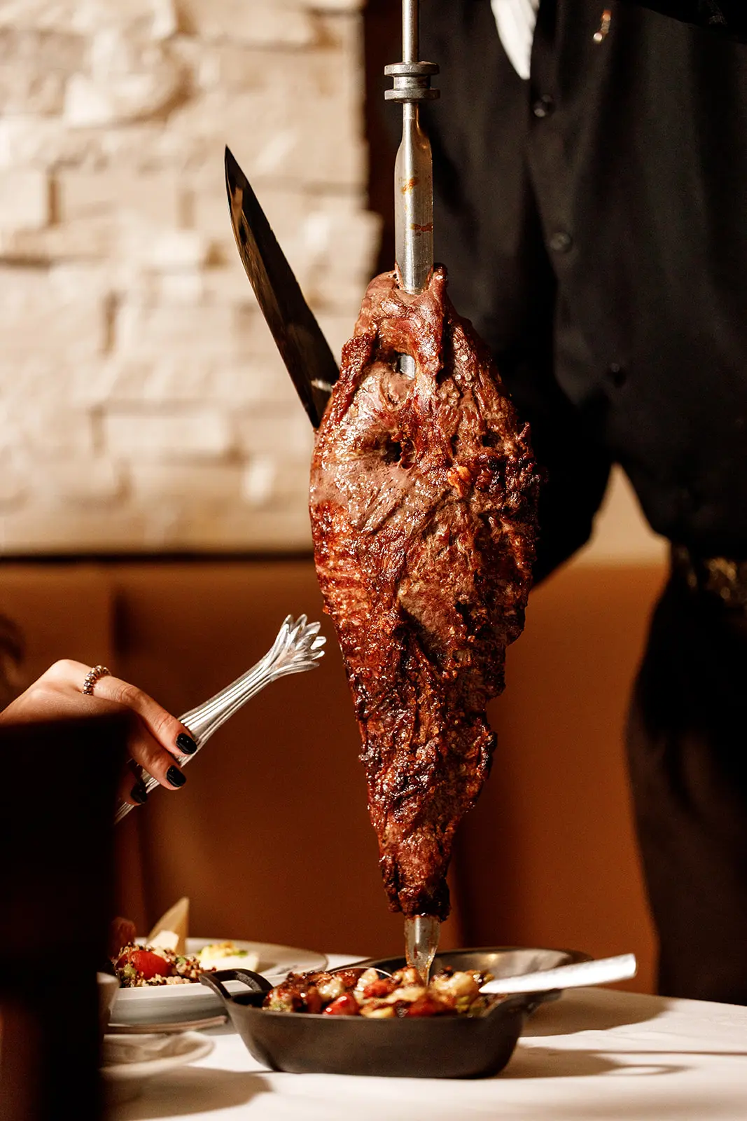 A gaucho carving fire-roasted beef from the skewer at the table during dinner