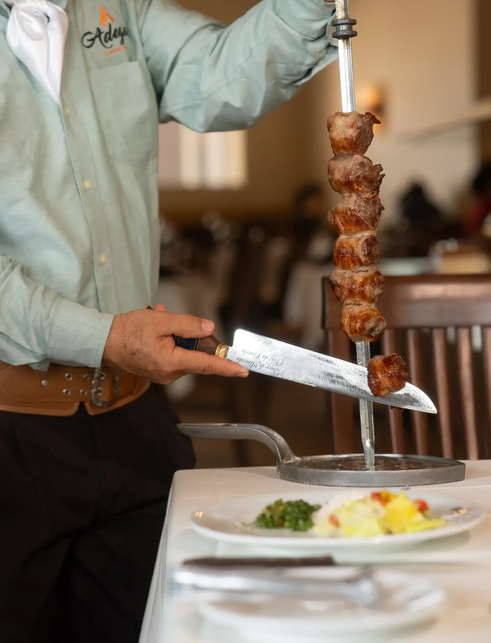 A gaucho carving fire-roasted meat from the skewer at the table during lunch
