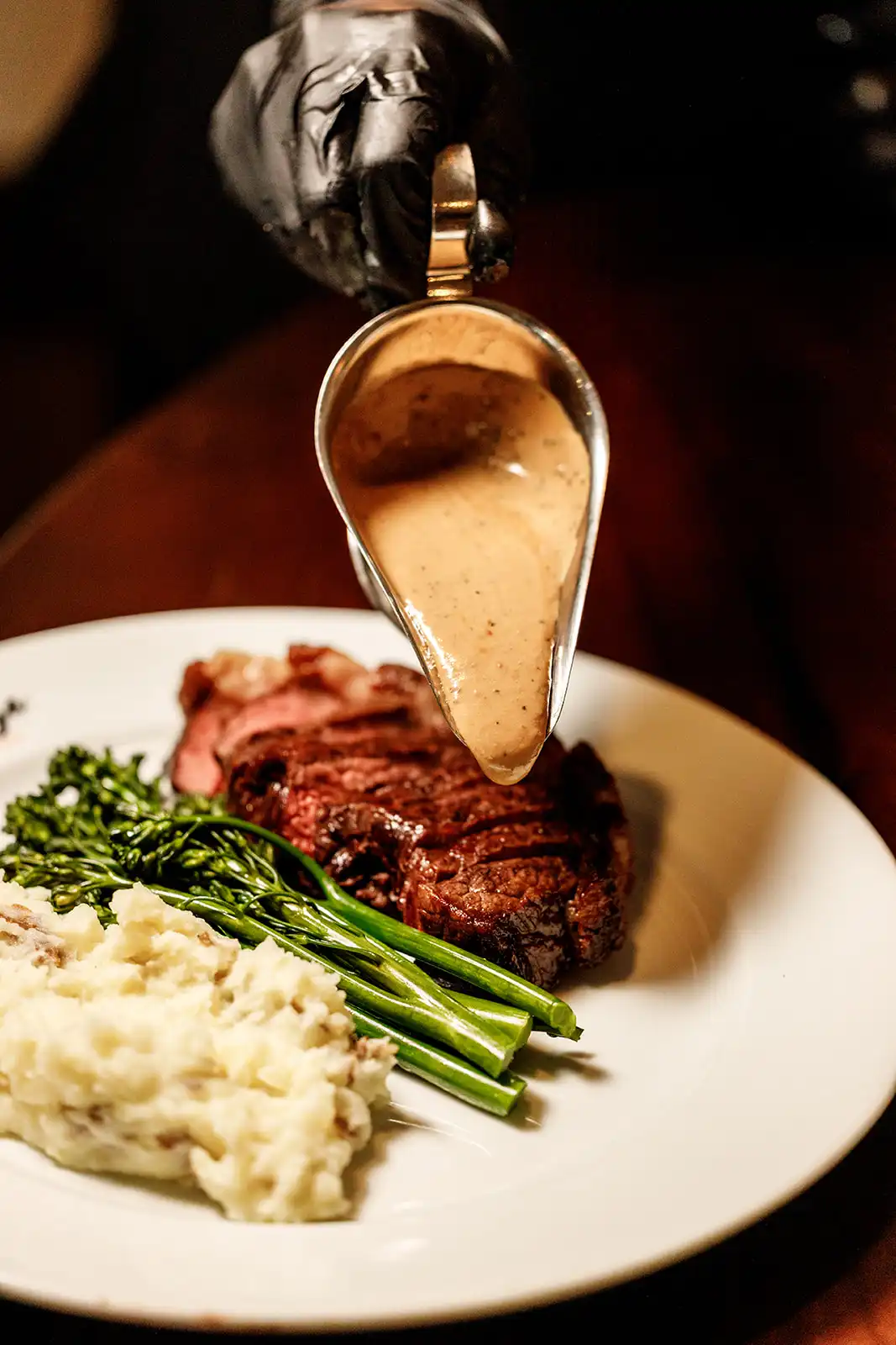 Peppercorn sauce poured over a grilled steak with broccolini and mashed potatoes